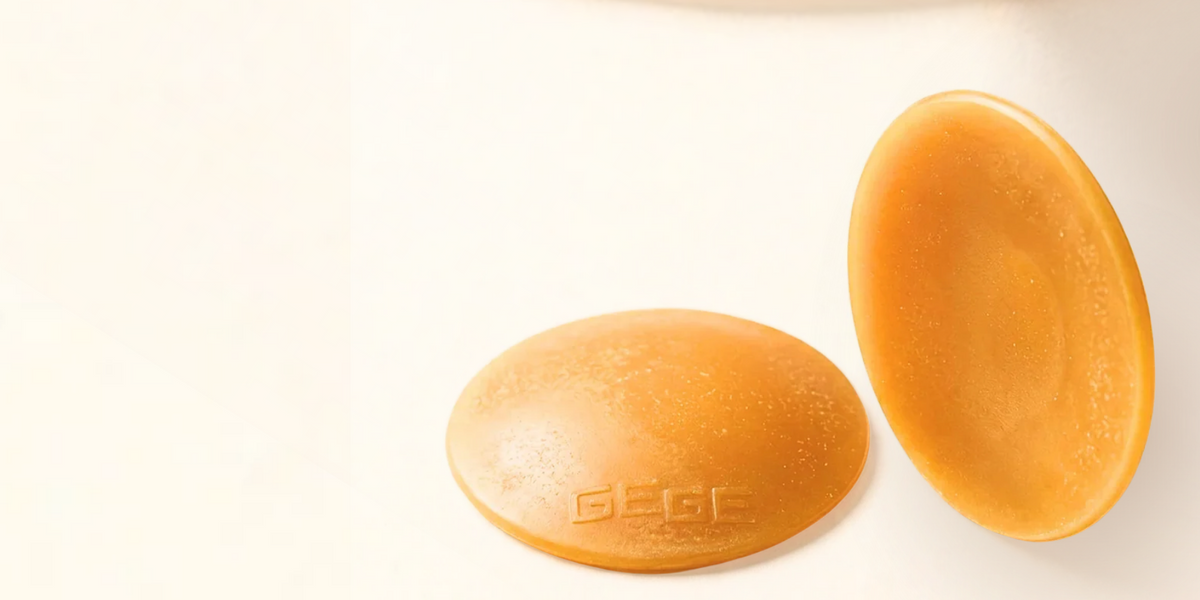 Two oval-shaped golden-yellow solid bars, likely beeswax or tallow candles, shown on a clean white background. One bar is embossed with the brand name 'GEEC'.